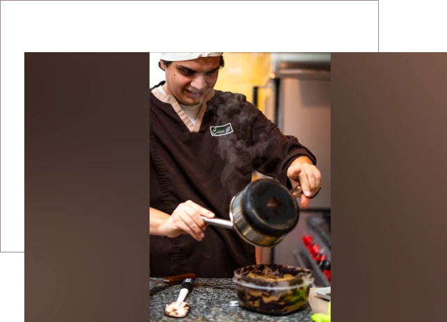 Chef pouring sauce over a dish in a kitchen.